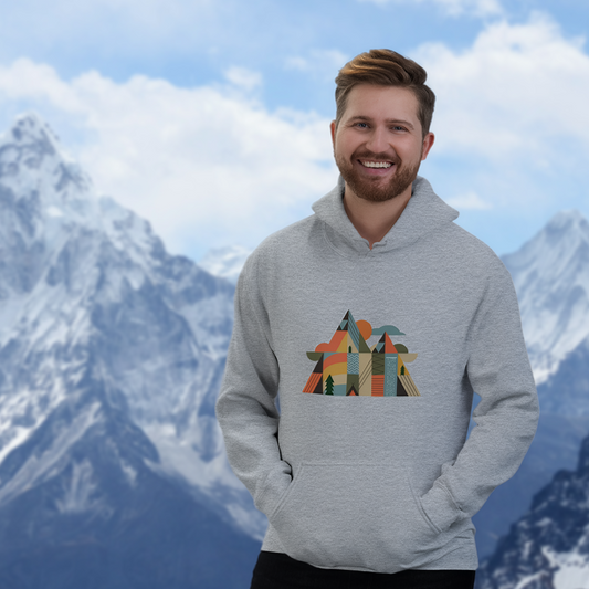homme en sweat à capuche gris illustré d’un motif montagne géométrique et coloré, debout face aux sommets en arrière-plan dans une ambiance outdoor