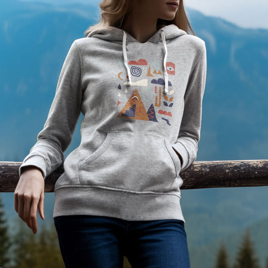 Sweat à capuche unisexe Sortie Longue porté en extérieur, personne appuyée sur un garde-corps avec vue montagne. Motif graphique central composé de pictogrammes paysage et outdoor.
