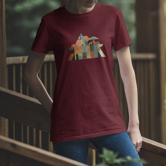 T-shirt unisexe Sortie Longue bordeaux porté en extérieur sur une passerelle en bois. Illustration bivouac et sommets graphiques sur la poitrine, tenue inspirée randonnée et plein air.