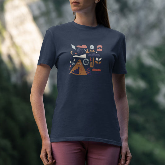 Femme portant un t-shirt unisexe Sortie Longue bleu marine, motif pictogrammes montagne et campement au centre. Photo portée en extérieur, look randonnée/voyage, idée cadeau pour marcheur et amateur de plein air.