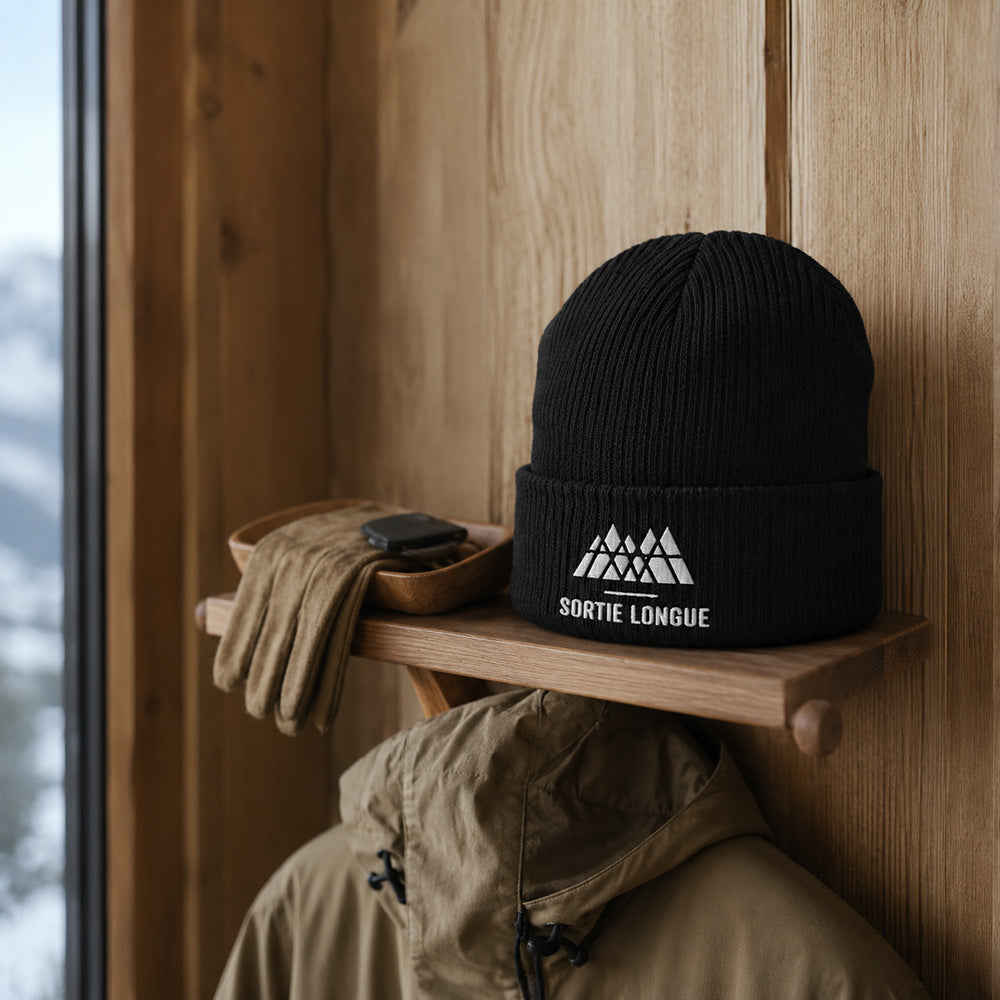 Bonnet tricoté coton bio logo Sortie Longue posé dans une entrée de chalet à l’ambiance rustique