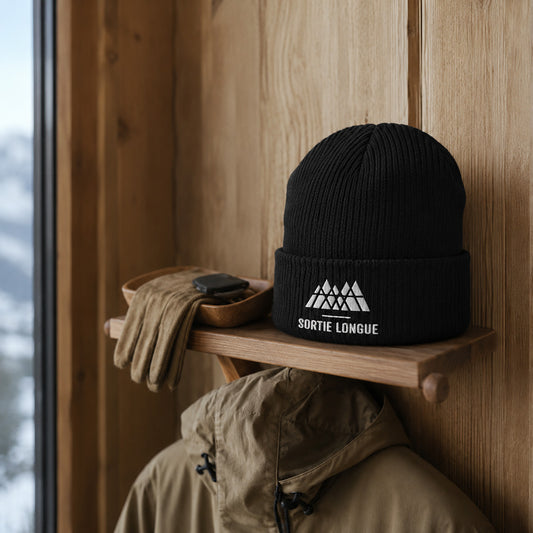 Bonnet tricoté coton bio logo Sortie Longue posé dans une entrée de chalet à l’ambiance rustique