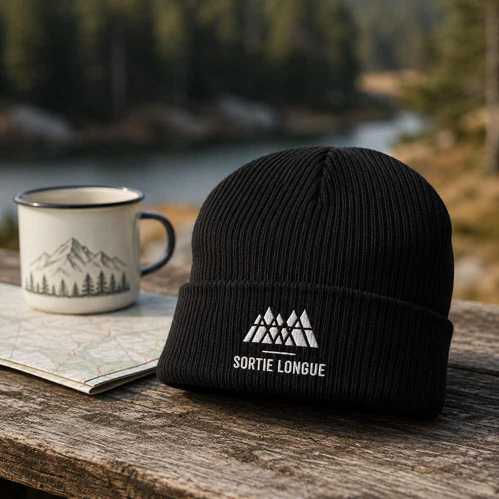 Bonnet tricoté coton bio logo Sortie Longue posé sur un équipement de randonnée en forêt