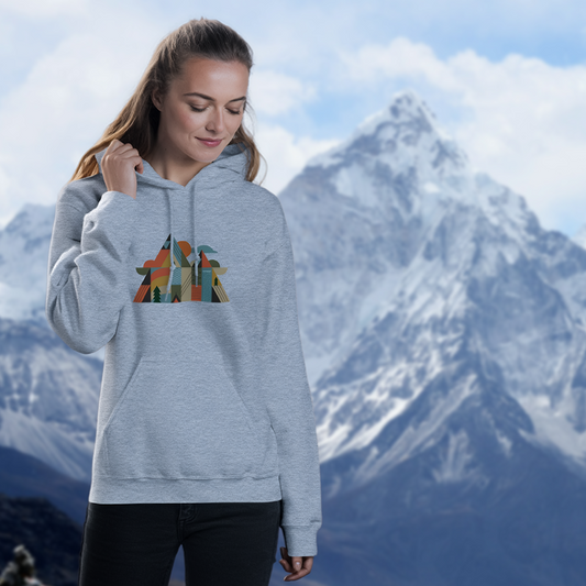 femme portant un sweat à capuche gris avec un design géométrique et coloré de montagnes, posant en extérieur devant un paysage montagneux