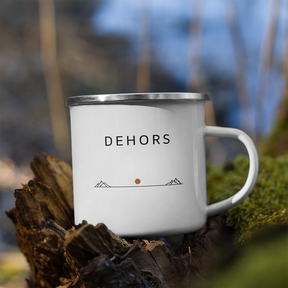 Mug Dehors Sortie Longue posé sur une roche en extérieur, avec design horizon sobre et typographie espacée.