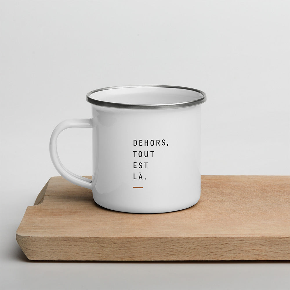 Mug Dehors posé sur une planche en bois avec la phrase Dehors, tout est là imprimée en typographie sobre.