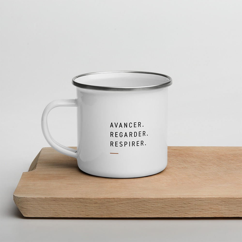 Mug émaillé blanc Dénivelé posé sur bois, avec la phrase Avancer Regarder Respirer imprimée en typographie sobre.