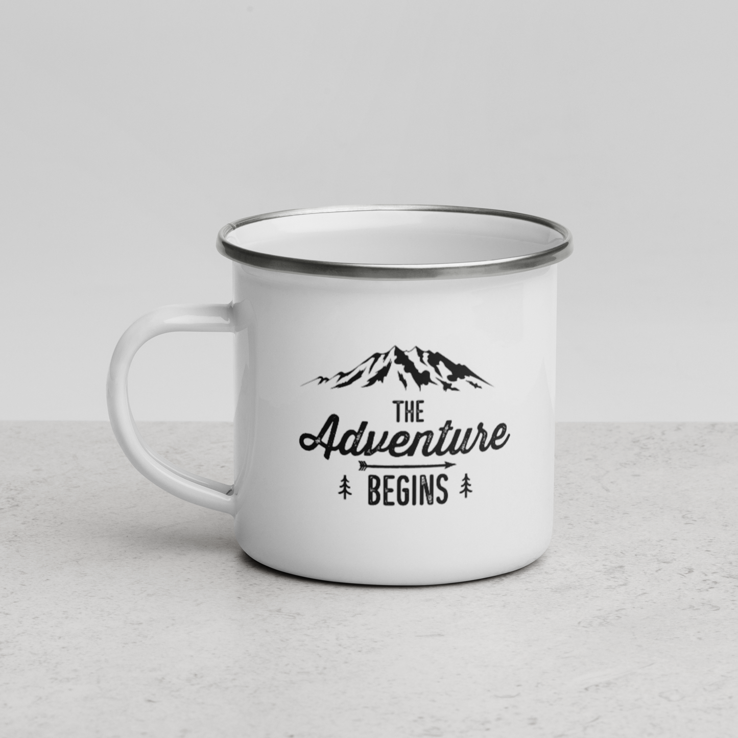 Mug métal émaillé Sortie Longue vu de face, design The Adventure Begins avec montagne dessinée, sapins et flèche directionnelle, visuel simple issu d’un moment réel avant la sortie.