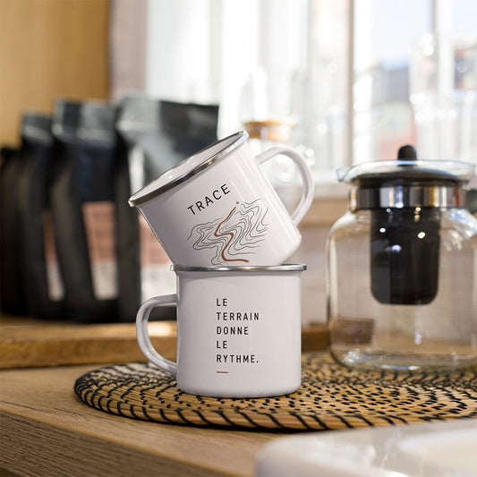 Deux mugs émaillés blancs Sortie Longue avec design Trace, l’un avec les courbes topographiques et l’autre avec la phrase Le terrain donne le rythme.