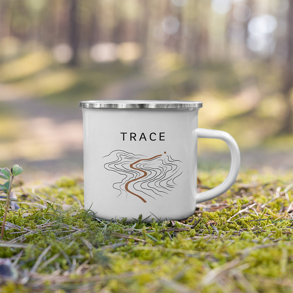 Mug émaillé Trace posé dehors sur la mousse, avec design topographique inspiré des sentiers, du relief et de l’univers outdoor.