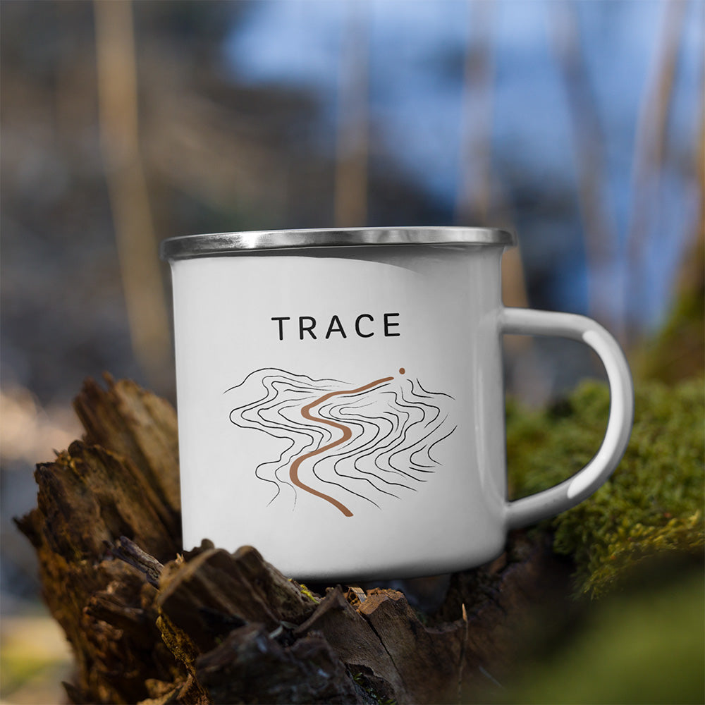 Mug Trace Sortie Longue posé sur une roche en extérieur, avec design topographique sobre et ligne de sentier couleur terre brûlée.