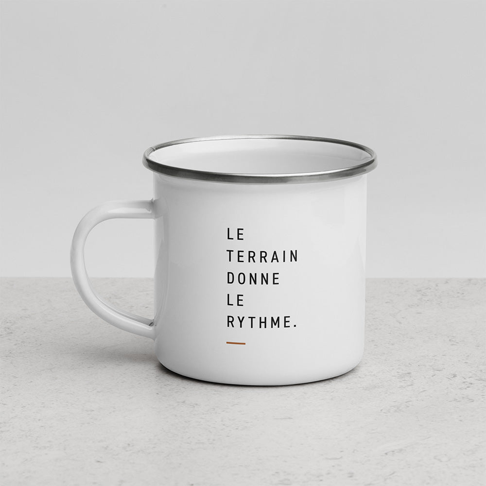 Mug émaillé blanc Sortie Longue avec la phrase Le terrain donne le rythme imprimée en typographie sobre sur fond clair.