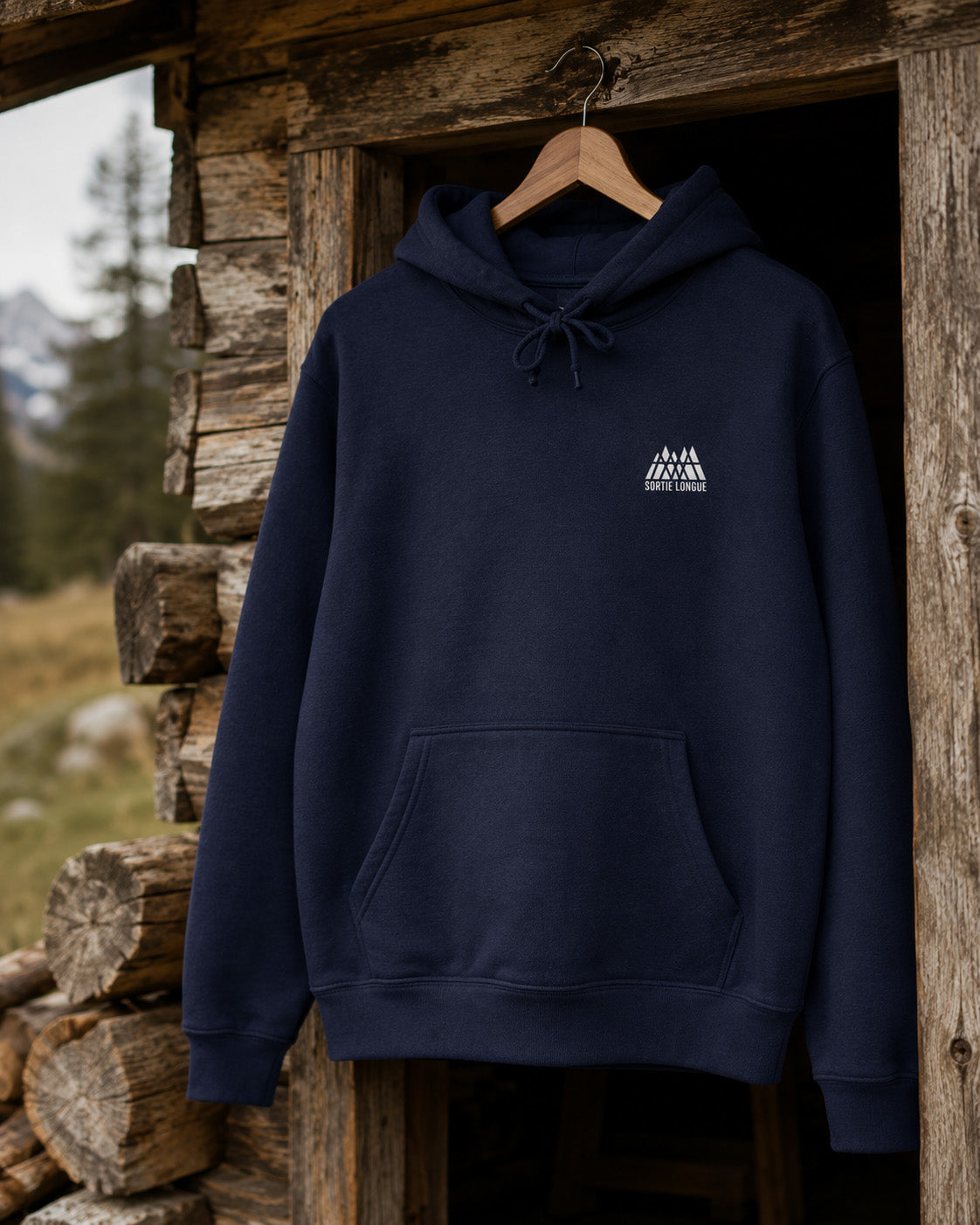 Sweat à capuche bleu marine Sortie Longue suspendu devant une cabane en bois en montagne
