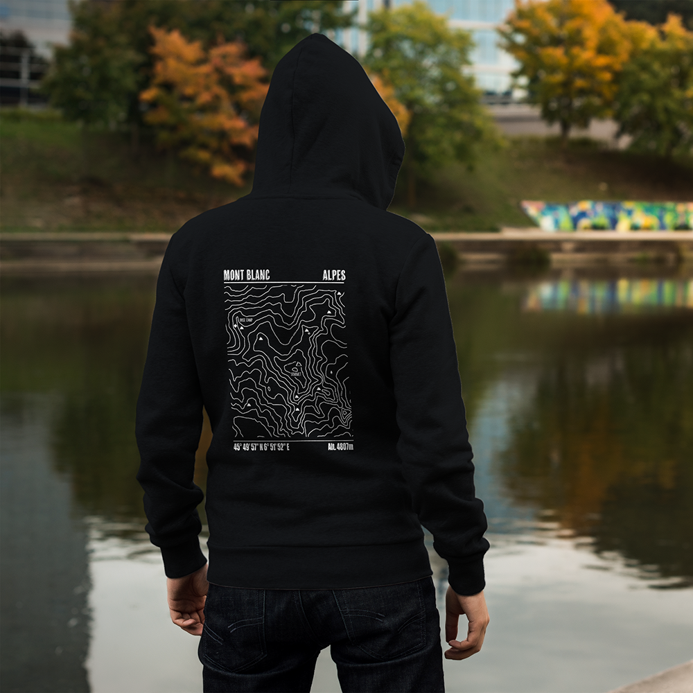 Sweat à capuche unisexe noir Sortie Longue porté en extérieur près d’un plan d’eau, vue de dos, impression carte topo Mont Blanc très visible, vêtement pour départ frais, approche et retour de sortie montagne.