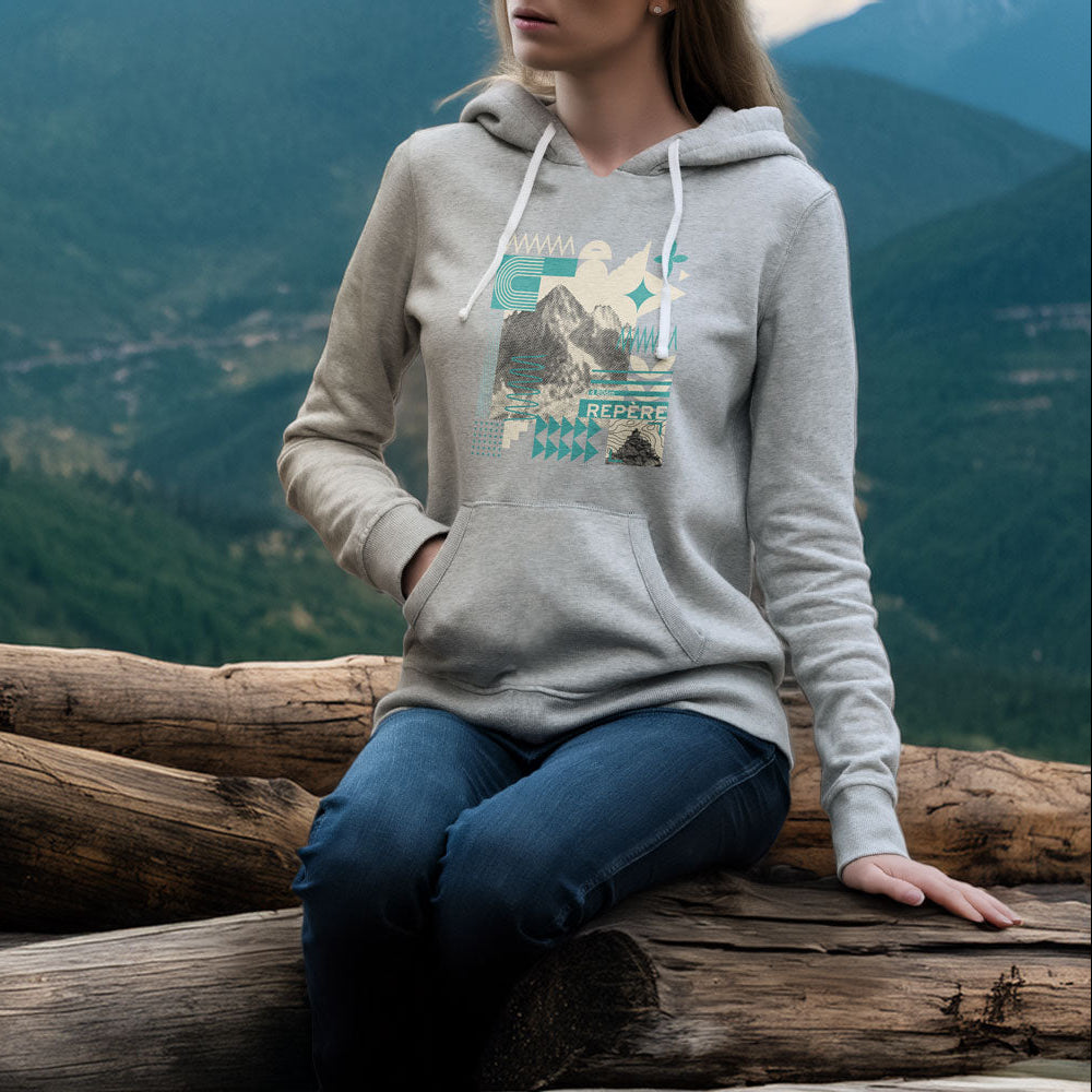 Sweat à capuche unisexe Sortie Longue porté en extérieur, personne assise sur un tronc en montagne. Motif central graphique inspiré de la lecture du terrain.