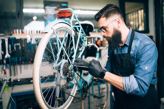 Tablier d’atelier Sortie Longue porté lors d’une réparation de vélo, contexte atelier mécanique, geste précis avant ou après une sortie vélo en extérieur.
