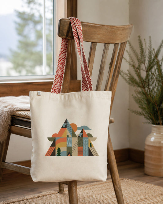 Tote bag recyclé Montagnes Géométriques Sortie Longue suspendu à une chaise en bois, ambiance intérieure naturelle avec lumière douce et esprit outdoor