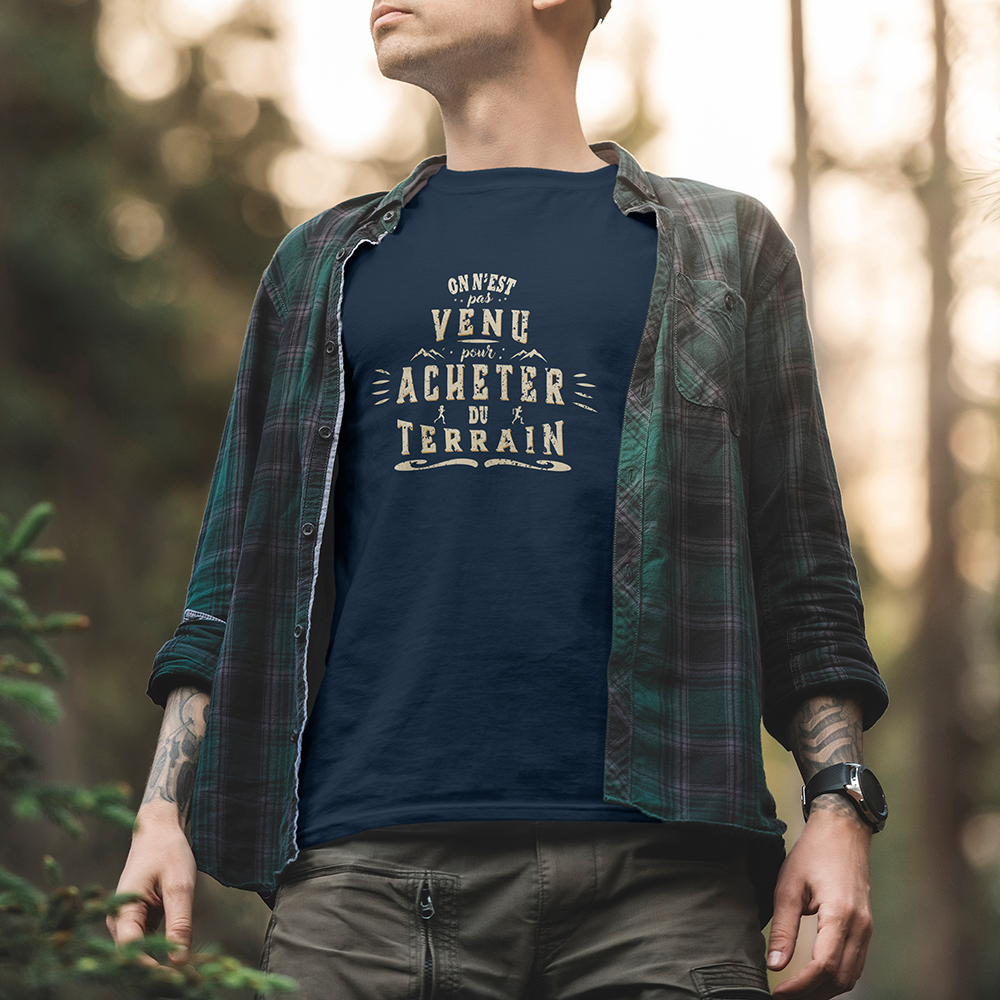 Modèle portant le t-shirt Sortie Longue bleu marine en extérieur, vue de face, texte « On n’est pas venu pour acheter du terrain » en typographie dense; t-shirt pour trail, trajets et quotidien.