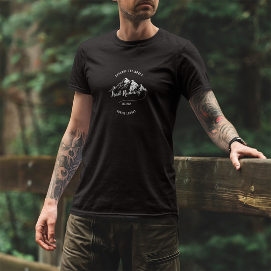 Modèle portant le t-shirt Sortie Longue noir en extérieur, vue de face, design « Explore the world » et « Trail running » avec chaîne de montagnes stylisée; tenue pour marche, sentier et déplacements.