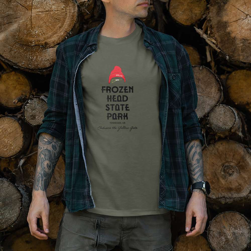 Modèle portant le t-shirt Sortie Longue kaki en extérieur, vue de face, texte « Frozen Head State Park » et slogan « Embrace the Yellow Gate » sous un bonnet rouge; pièce unisexe esprit ultra-trail.