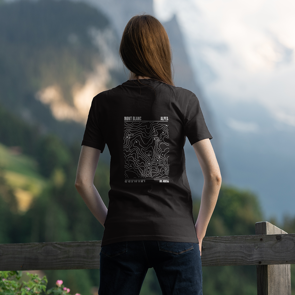 T-shirt unisexe Sortie Longue noir porté, vue de dos en extérieur face aux montagnes, grande carte topographique du Mont Blanc imprimée, courbes de niveau; tenue rando, trail, tour du Mont Blanc.