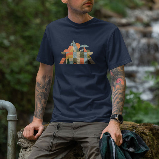 Homme portant un t-shirt unisexe Sortie Longue bleu marine, motif bivouac et montagnes stylisées au centre. Photo portée en extérieur près d’une cascade, ambiance nature et randonnée.
