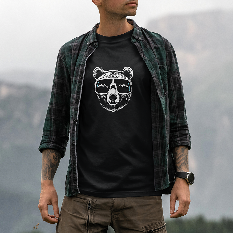 Modèle portant le t-shirt Sortie Longue noir en extérieur, vue de face, t-shirt ours montagne avec ours avec lunettes et reflet de relief; pièce unisexe pour trail et quotidien.