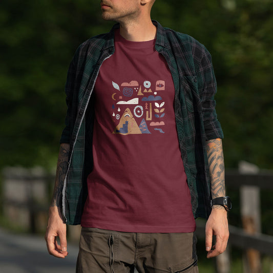 Homme portant un t-shirt unisexe Sortie Longue bordeaux, motif pictogrammes montagne/bivouac au centre, surchemise ouverte. Photo portée en extérieur, tenue randonnée/trail, idée cadeau outdoor.