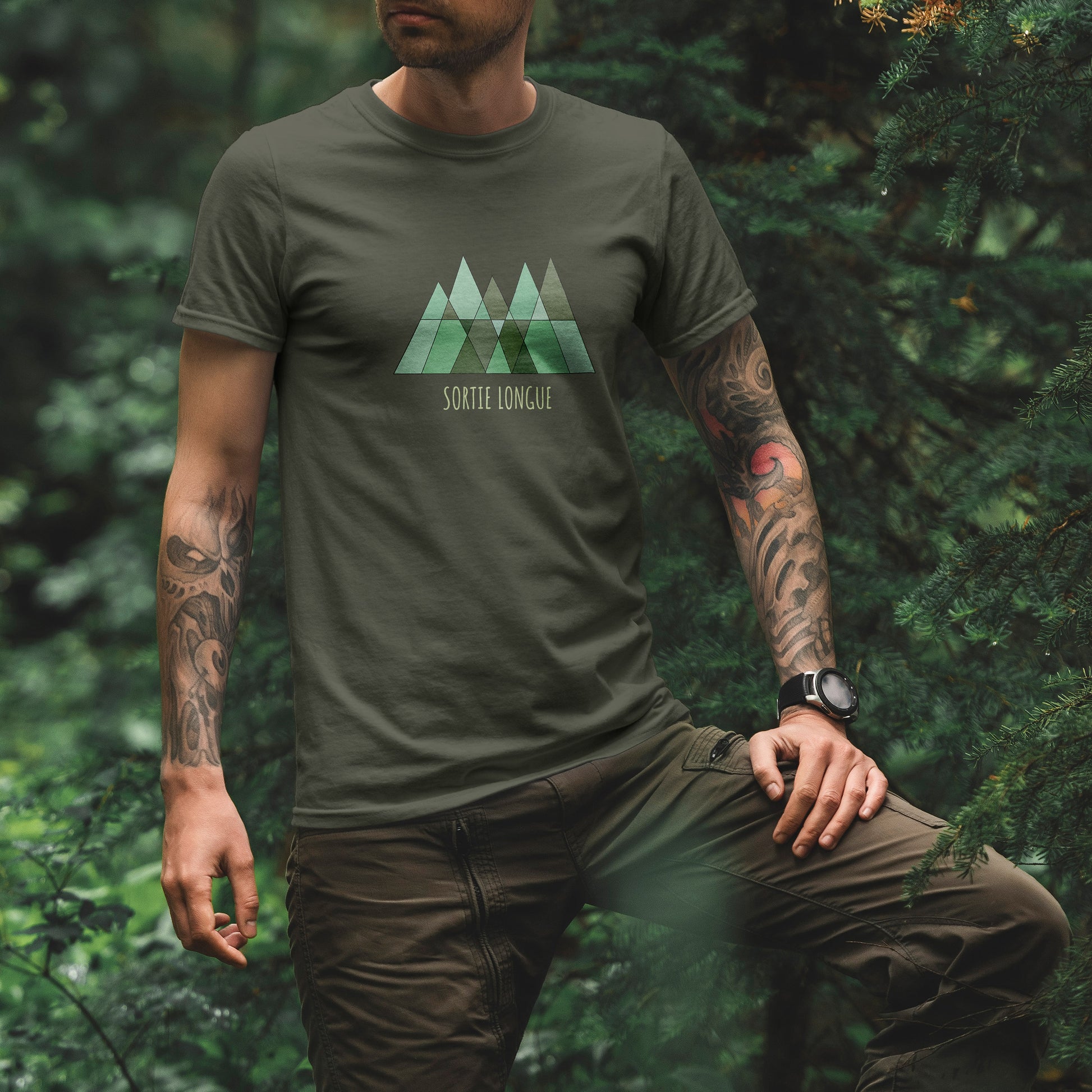 T-shirt unisexe Sortie Longue kaki porté en forêt, vue de face, logo triangles verts imprimé avec texte Sortie Longue, tenue sobre pour marche, sentier et sorties dehors.